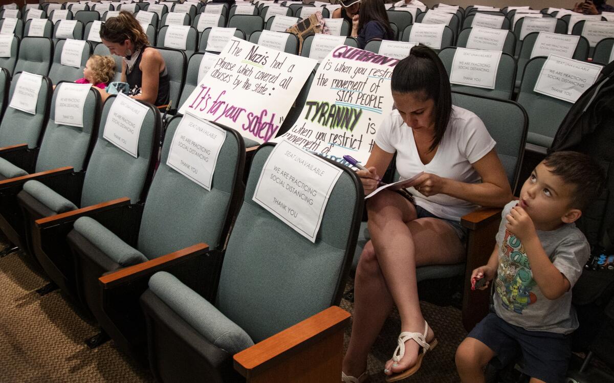 Jessica Schuurnans writes down comments she will present to the Riverside County Board of Supervisors during its emergency meeting. Friday. "It's time to open California, " she said. She also brought along the posters on the left.