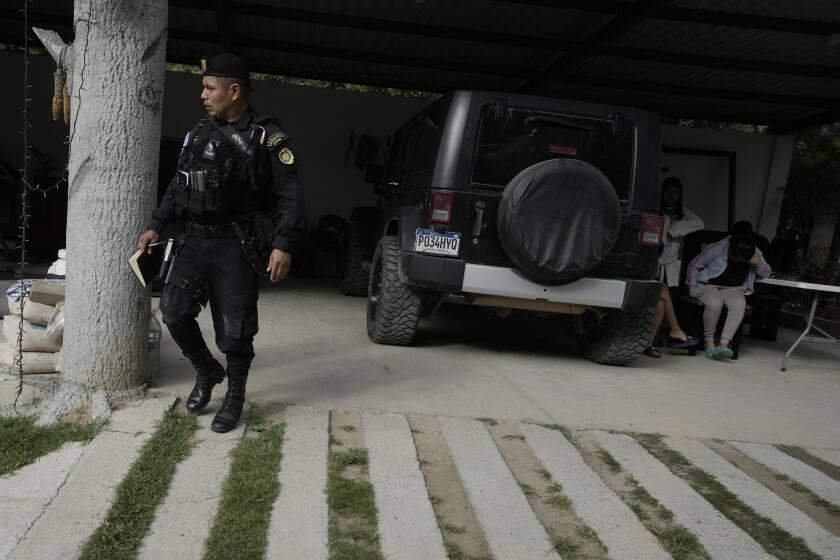 A Guatemalan police officer walks near alleged human traffickers, far right, who covered their faces, during a police raid against migrant smugglers near the Mexican border in Huehuetenango, Guatemala, Tuesday, Aug. 2, 2022. (AP Photo/Moises Castillo)