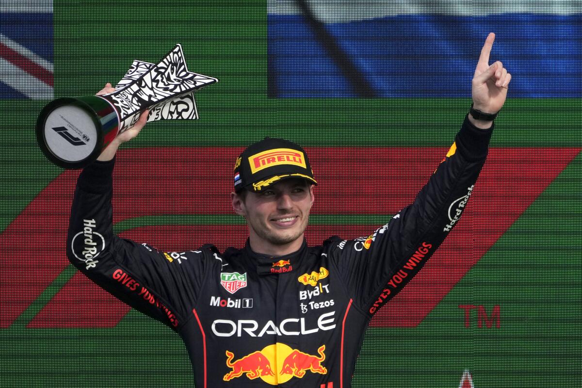 Max Verstappen lifts his trophy on the podium and holds up an index finger.