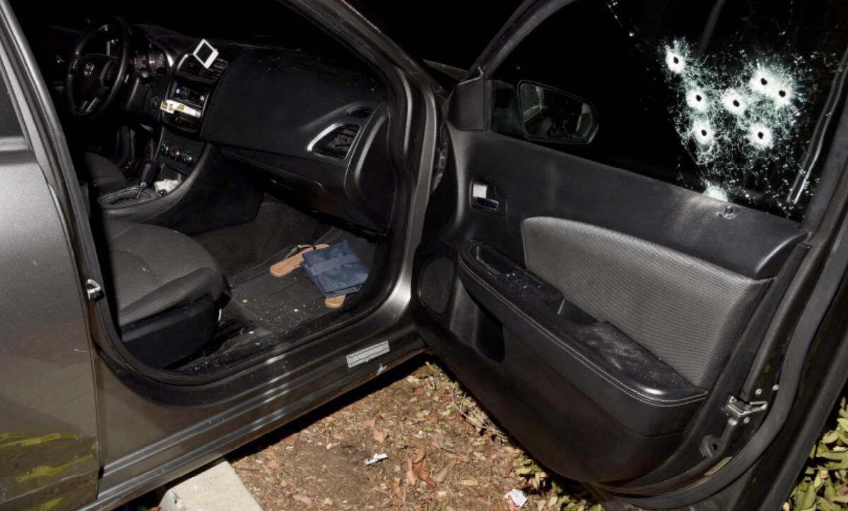The passenger-side door of a crashed Dodge Avenger with seven bullet holes in the window