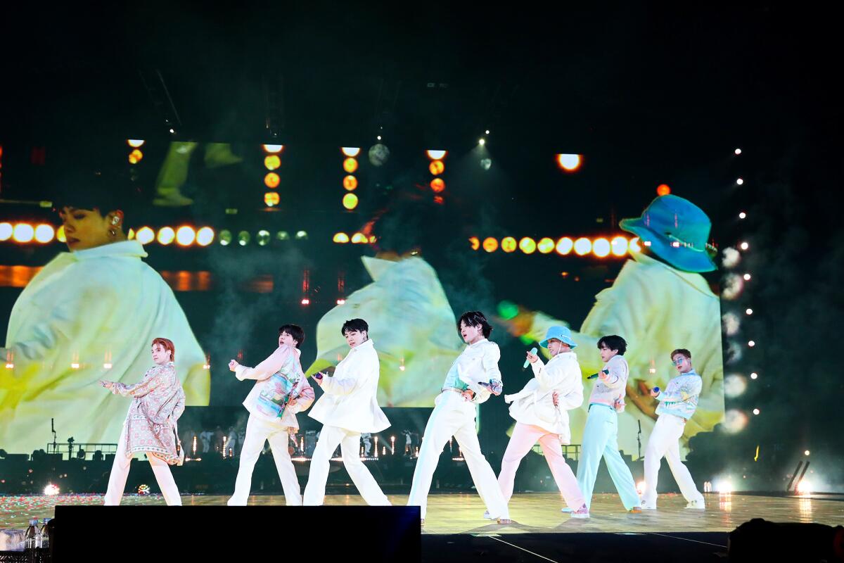 Seven men in matching white suits dance on a stage