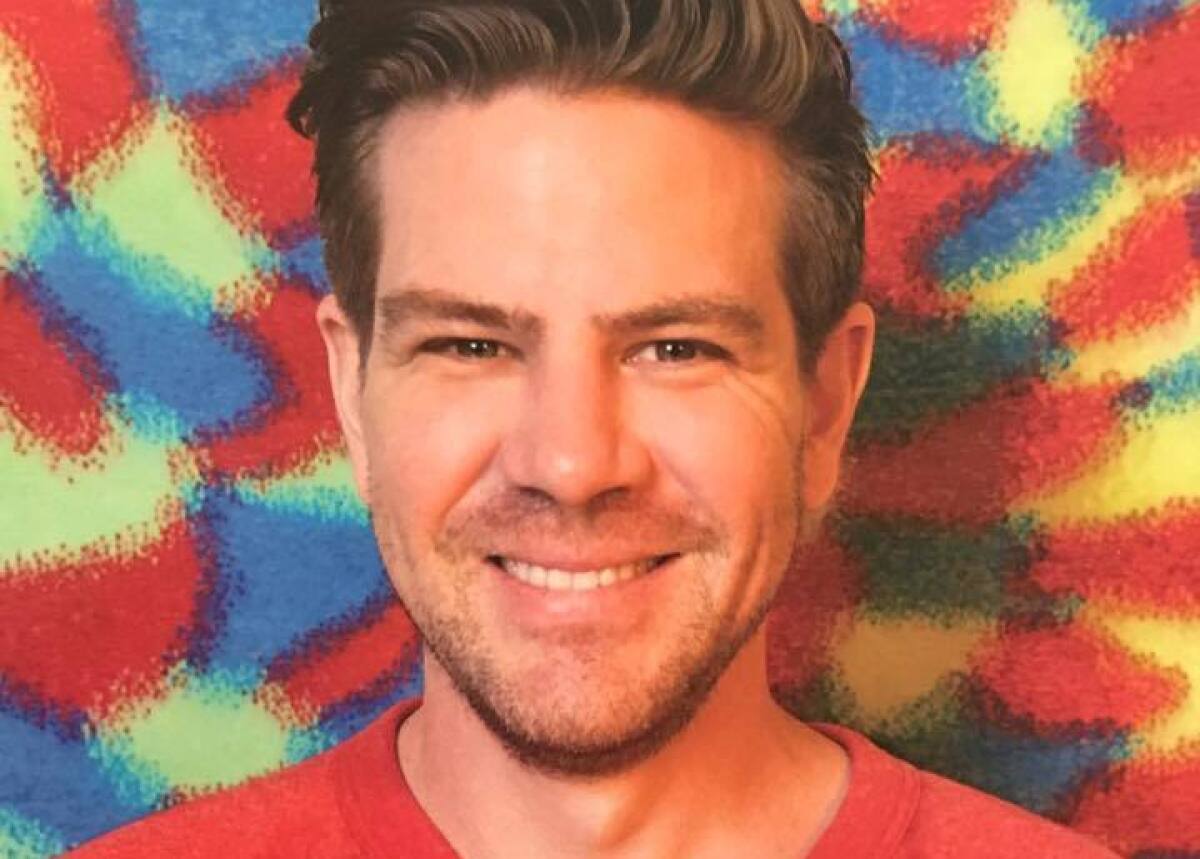 Man in a red shirt in front of a tie dye background 