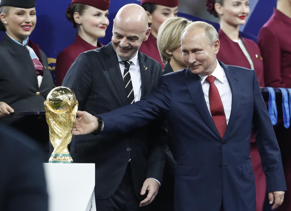 Russian President Vladimir Putin touches the World Cup trophy as FIFA President Gianni Infantino stands beside him