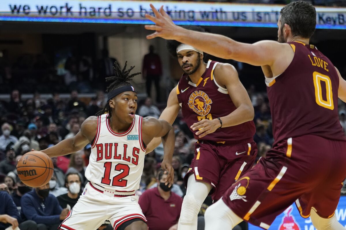 Chicago Bulls' Ayo Dosunmu (12) drives against Cleveland Cavaliers' Jarrett Allen (31) and Kevin Love (0) in the first half of an NBA basketball game, Wednesday, Dec. 8, 2021, in Cleveland. (AP Photo/Tony Dejak)