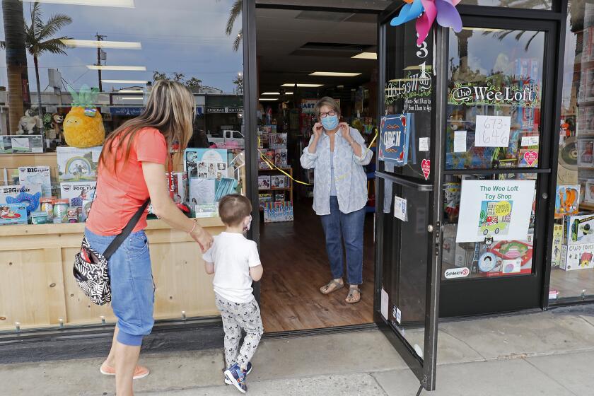 Owner Erin Kelly, right, adjusts her face mask as she welcomes longtime customer Eva Stellar, left, with her son Jake, 4, at The Wee Loft, an independent toy store in Corona del Mar on Friday, May 8. Gov. Gavin Newsom on Thursday announced Phase 2 of his stay-at-home order, allowing for some retailers to reopen but not have customers in stores amid the coronavirus pandemic. Businesses such as toy stores, florists, clothing stores and book stores were allowed to reopen for curbside pickup.