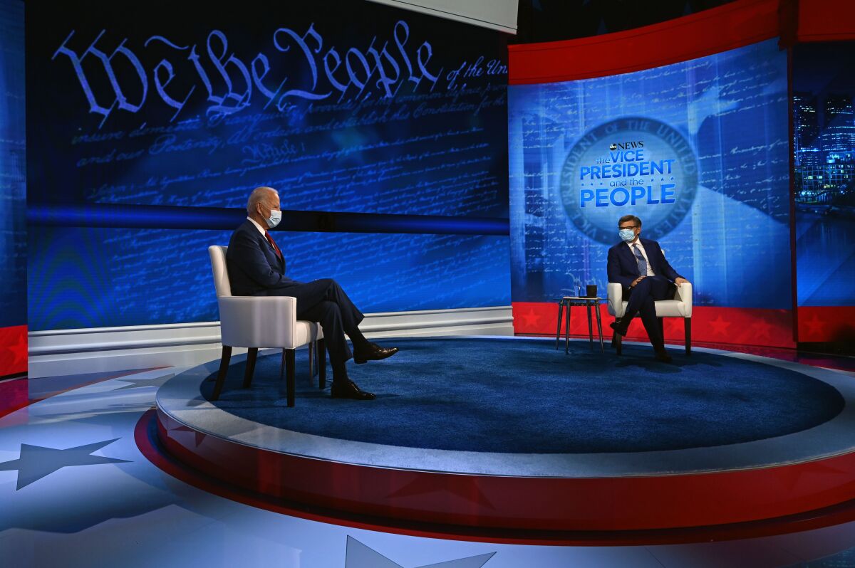 Joe Biden sits across a stage from the moderator in front of a wall with graphics of the Constitution