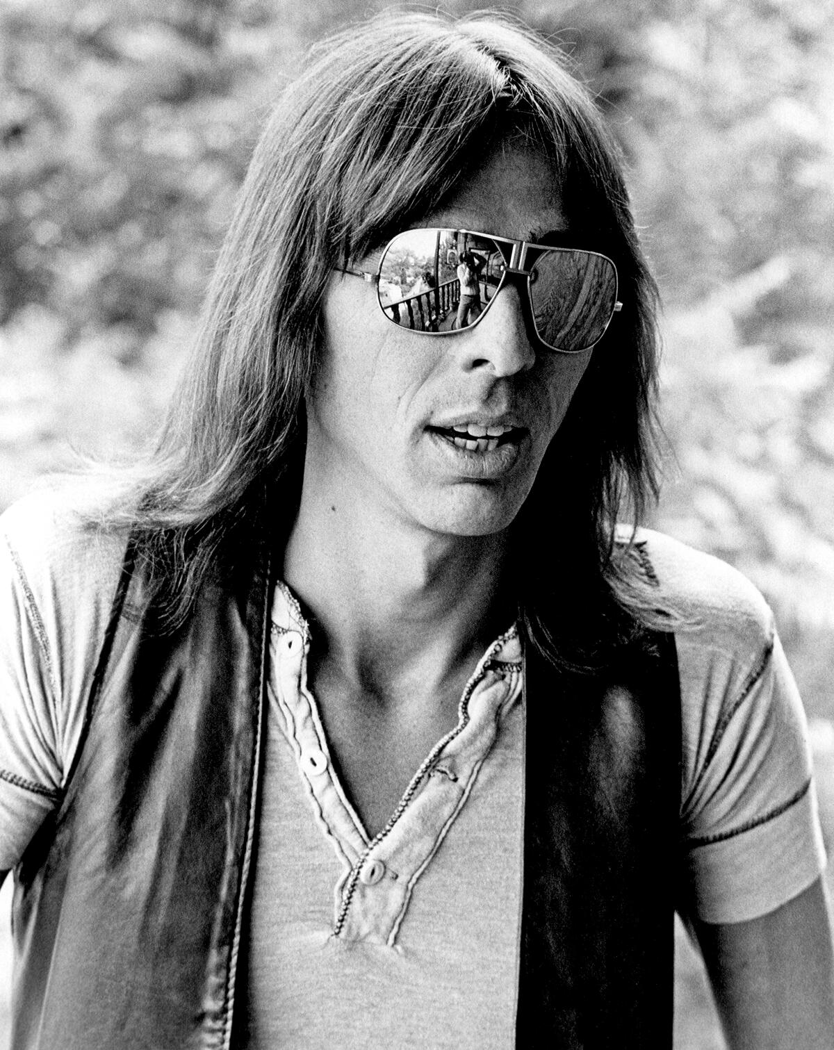 A long-haired man in sunglasses, open-necked shirt and leather vest