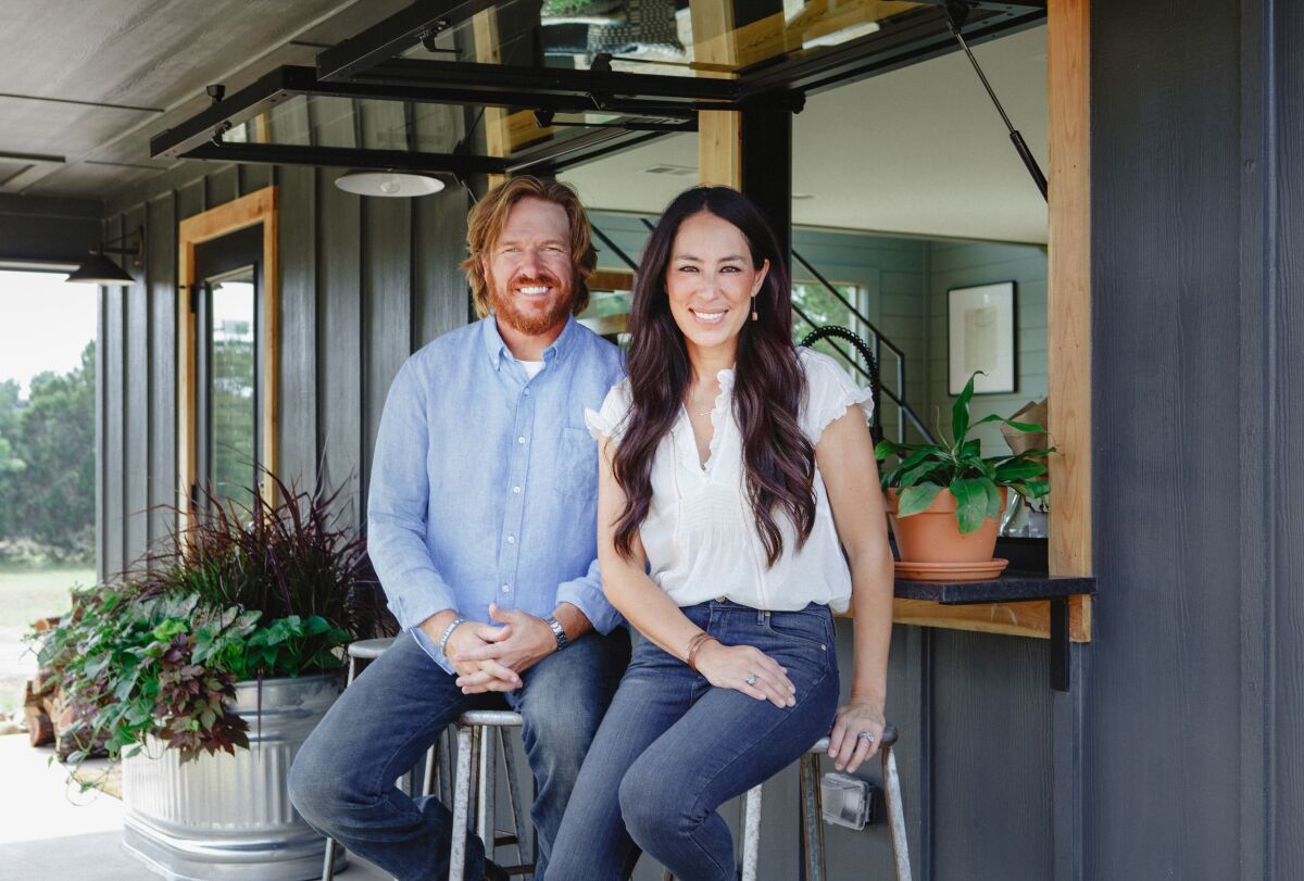 A man and a woman sit on stools in front of a completed renovation