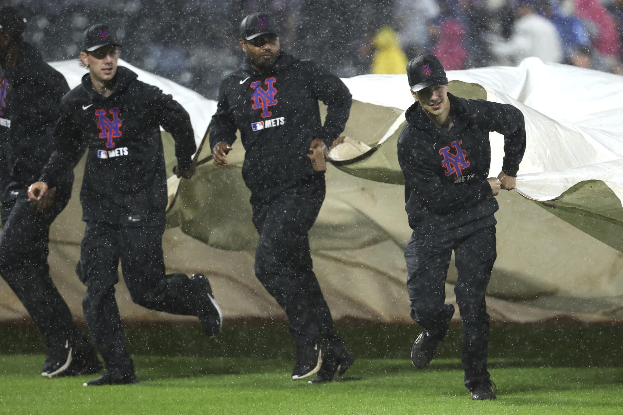 Los miembros de la tripulación del terreno cubren el campo durante un retraso de lluvia en Citi Field el viernes por la noche.