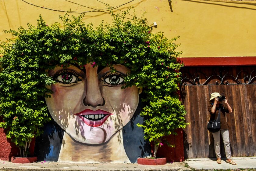 A tourist stands beneath a mural in San Miguel de Allende, Mexico.