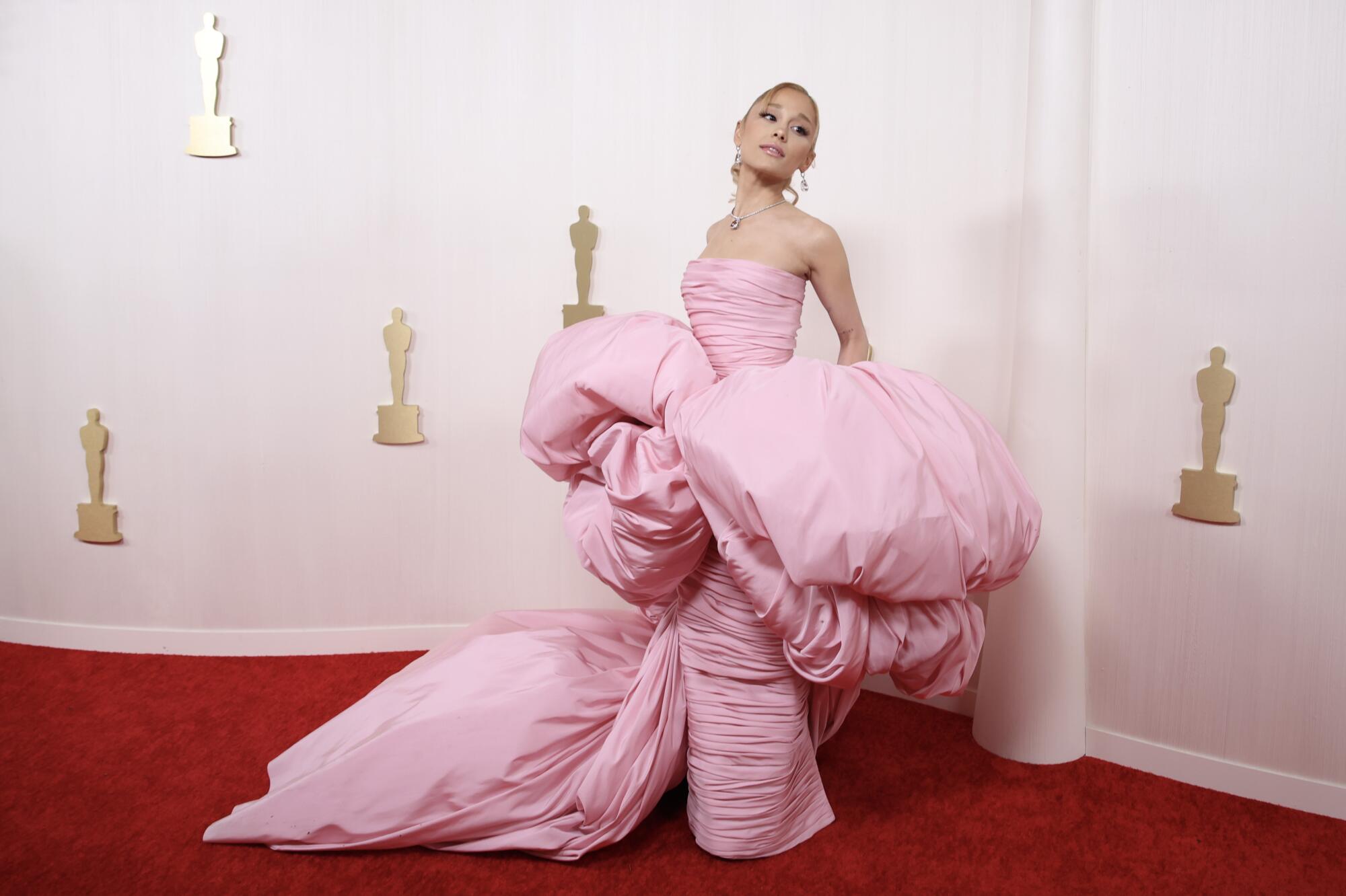 Ariana Grande wears a light pink ruched column gown with a voluminous cape.  
