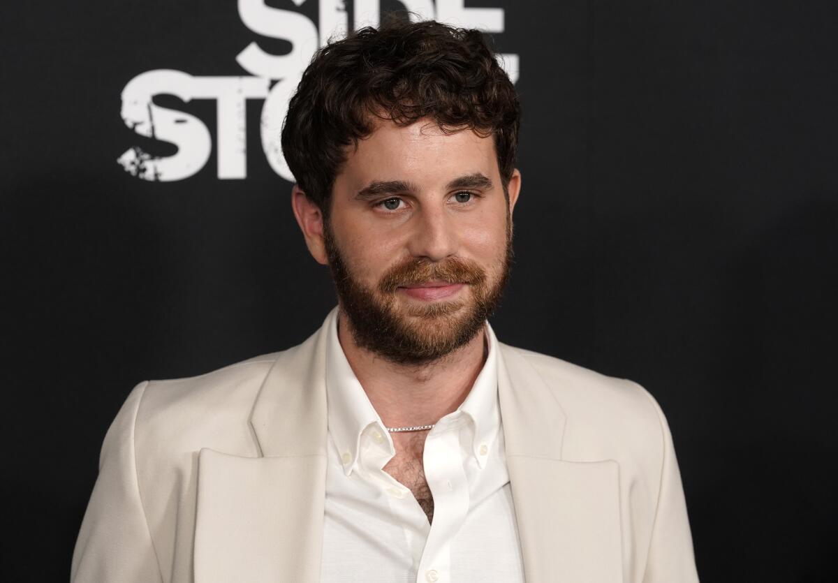 A man with brown hair and facial hair wearing a beige suit poses for pictures