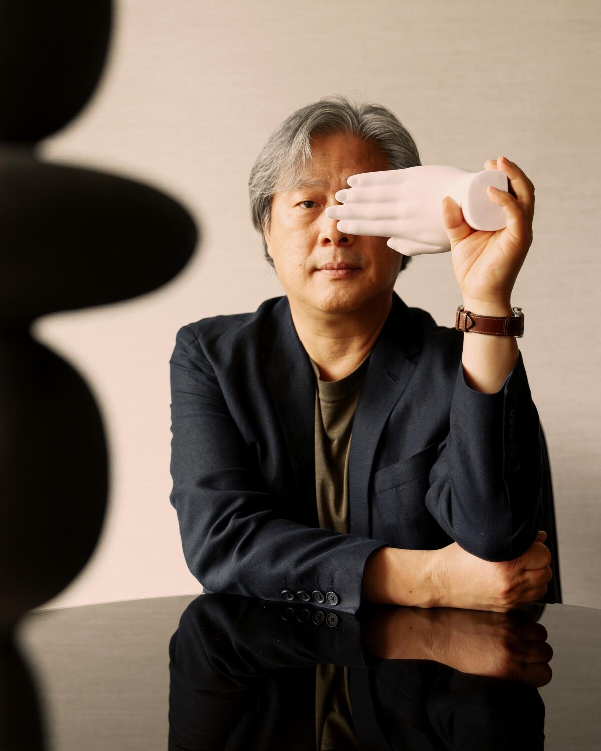 Park Chan-wook poses for a portrait holding a fake hand over one eye.
