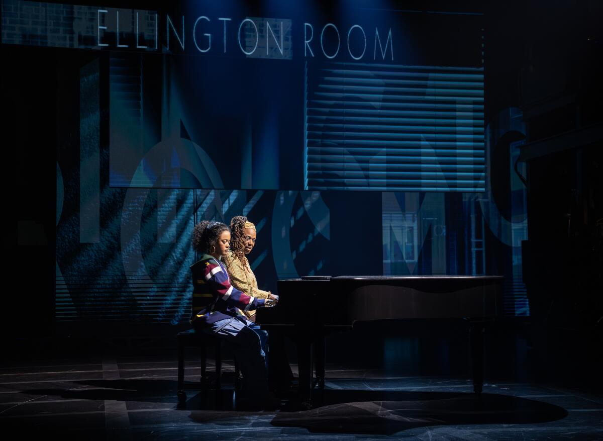 Two actors sit at a piano on a dark stage under the words "Ellington Room"