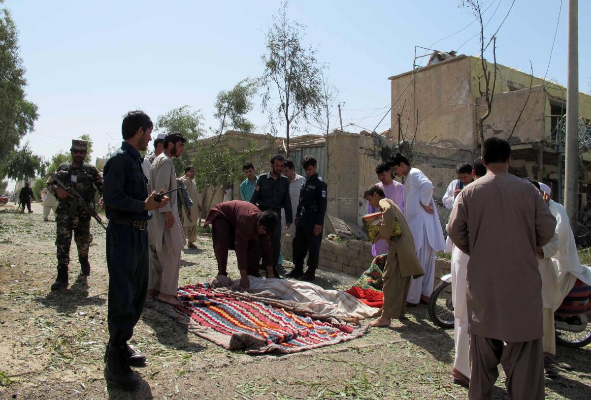 Afghan bystanders cover the body of a civilian after an attacker detonated a truck bomb targeting police headquarters in Lashkar Gah, Afghanistan, on June 30.