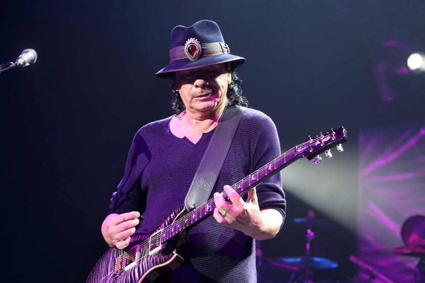 A man wearing a black hat looks down as he plays the guitar onstage