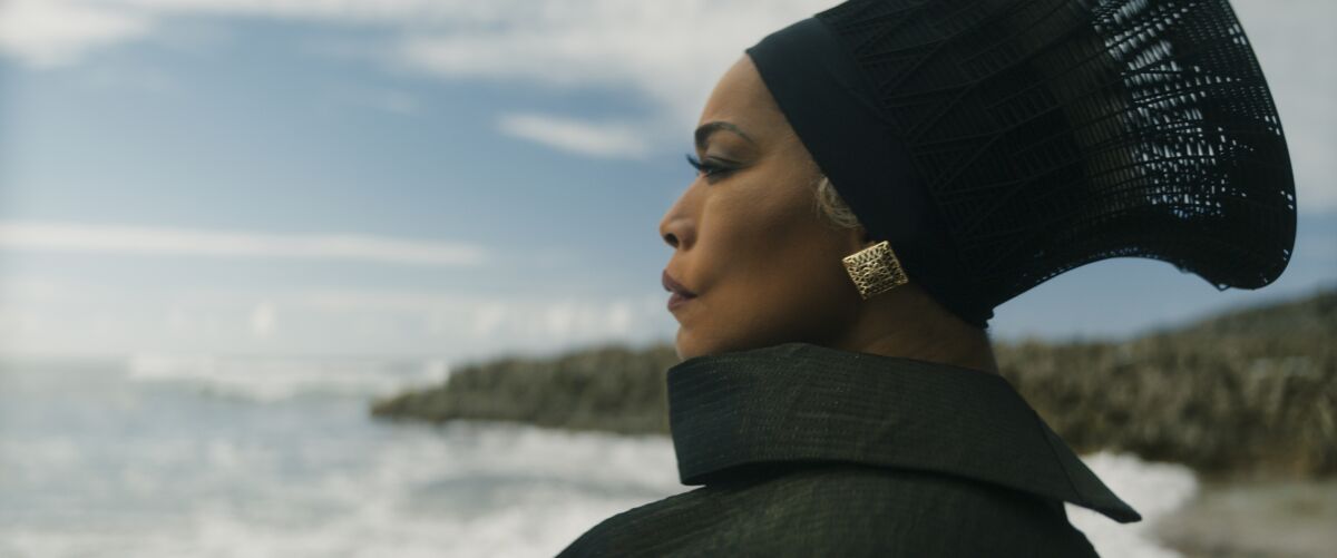 Angela Bassett looks out at the ocean wearing black headwear and high collar wrap in "Black Panther: Wakanda Forever." 