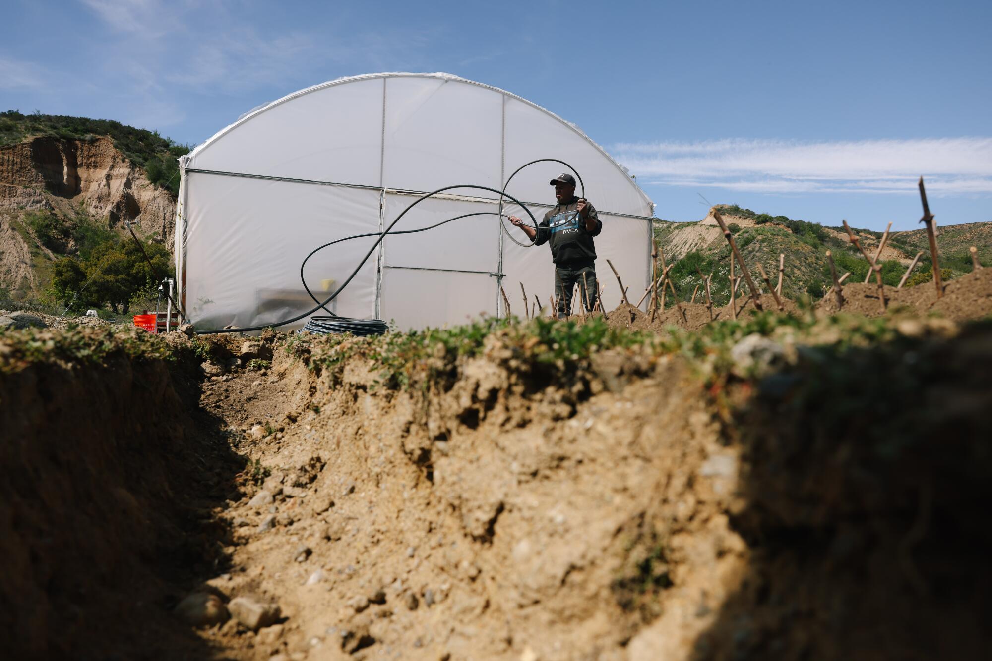 A man works outdoors next to a building and a large hole dug in the ground.