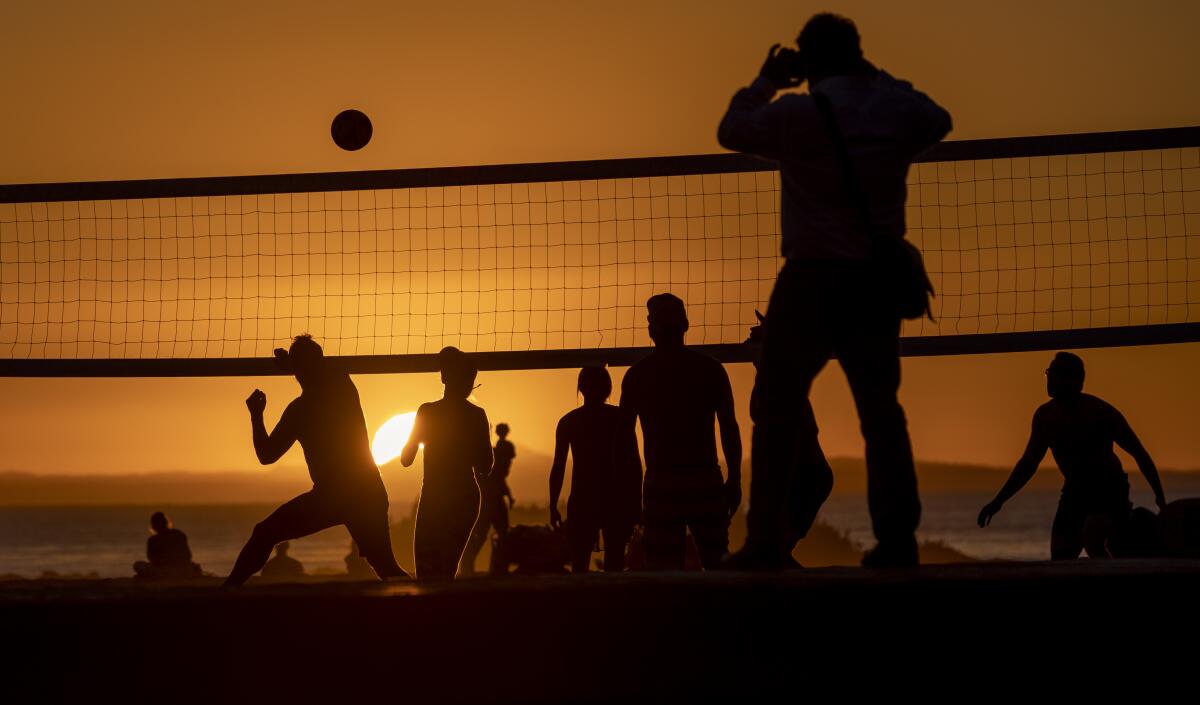 Against a dusk sky, a passerby photographs beach volleyball players on a warm February evening at Main Beach in Laguna Beach