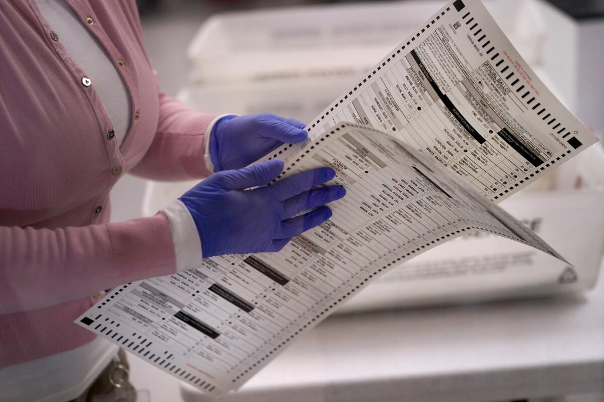 A close shot of a person's blue-gloved hands holding two ballots
