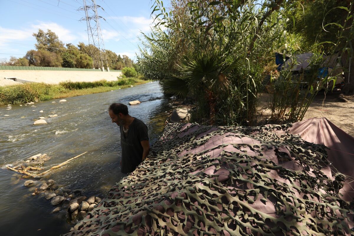 Tyrone Hart, 56, stands next to his camoflauged tent which on the bank of the Los Angeles River. He's been living on the river for 13 years.