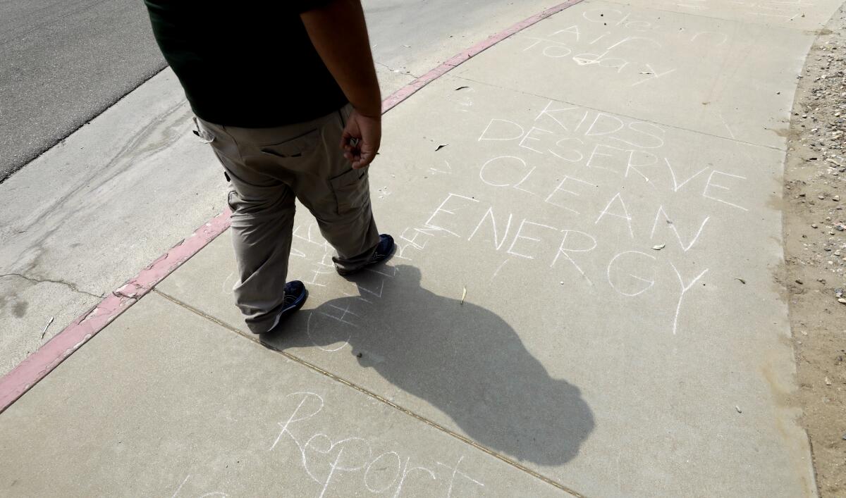 A pedestrian passes messages chalked on a sidewak, including "KIDS DESERVE CLEAN ENERGY."