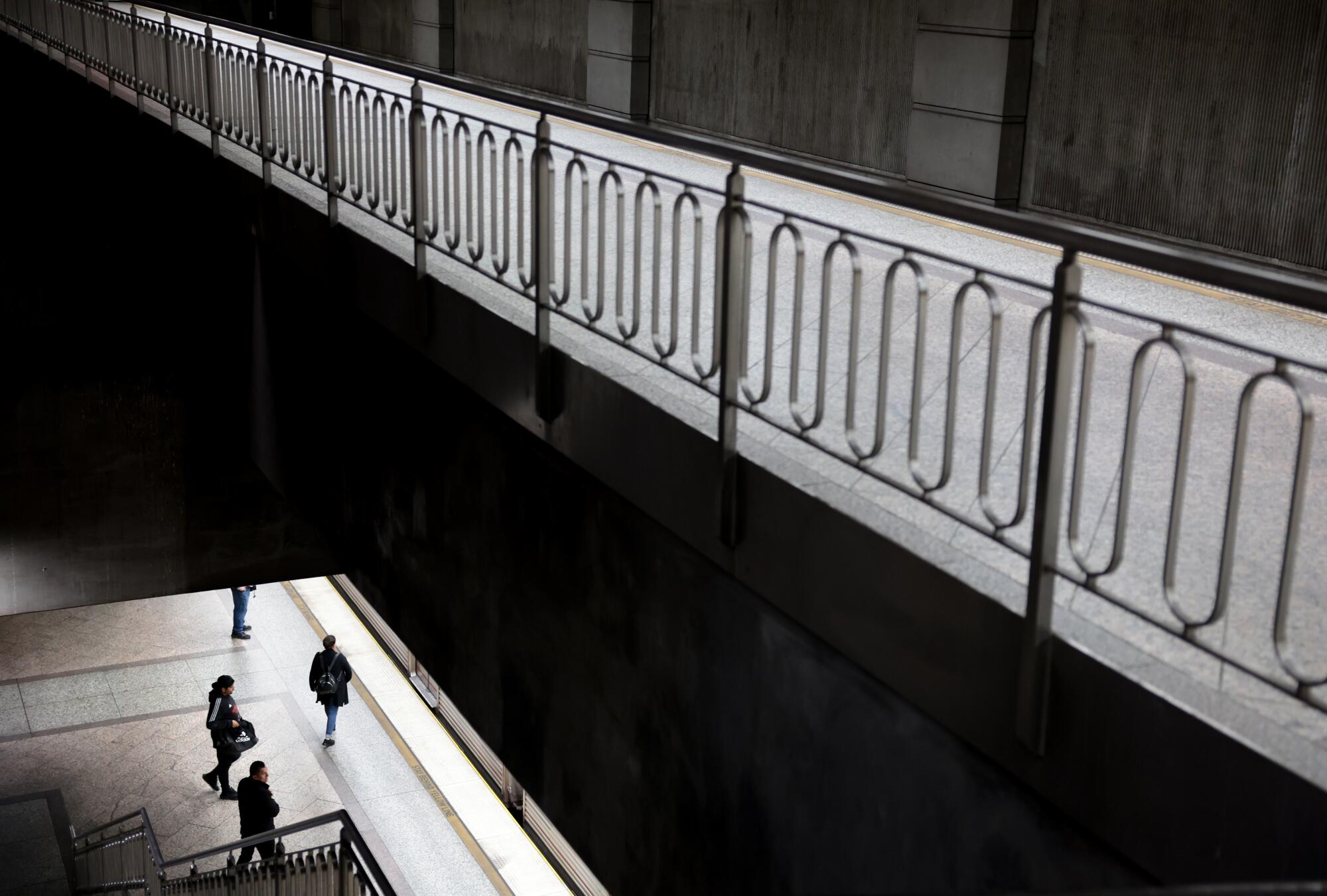 People walking on a lower level of a transit station are seen from above.