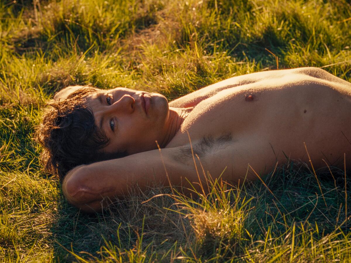 A shirtless young man lies back on the grass in "Saltburn."