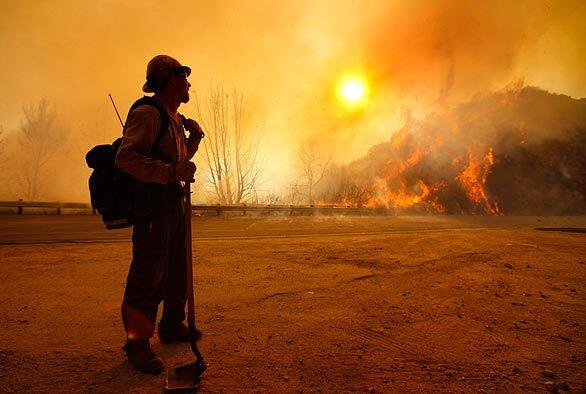 Firefighter Scott Allen glances across Angeles Crest Highway as canyon winds whip up flames at sunrise.