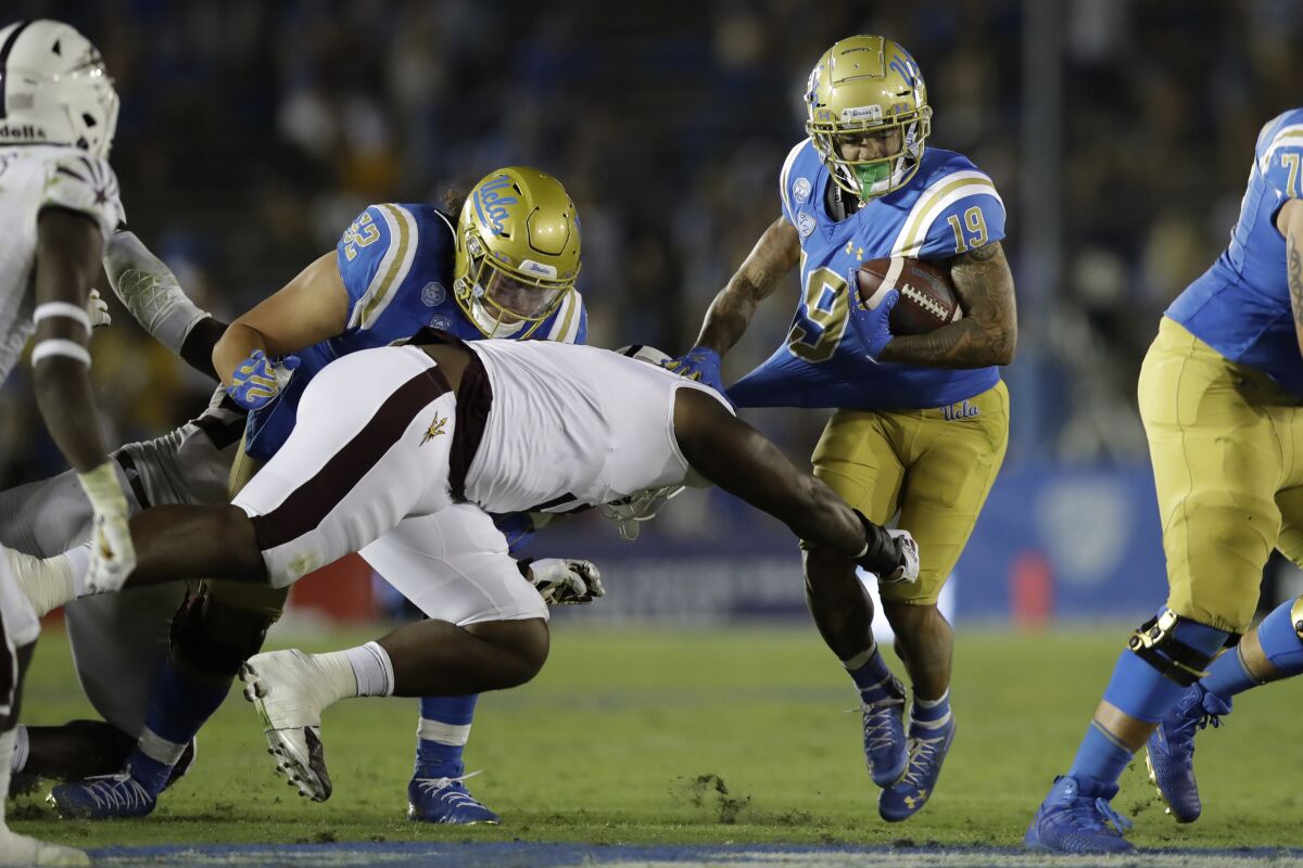 UCLA running back Kazmeir Allen has his jersey pulled as a defender dives toward his legs while he runs with the ball.