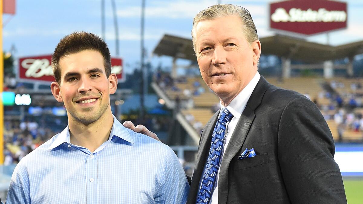 Dodgers broadcasters Joe Davis and Orel Hersheiser pose on the field together before a game.