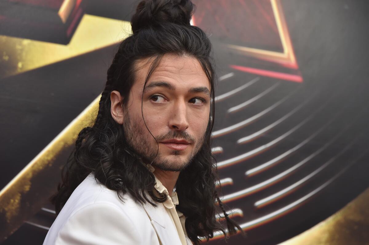 Ezra Miller looks over their shoulder while wearing a white blazer.