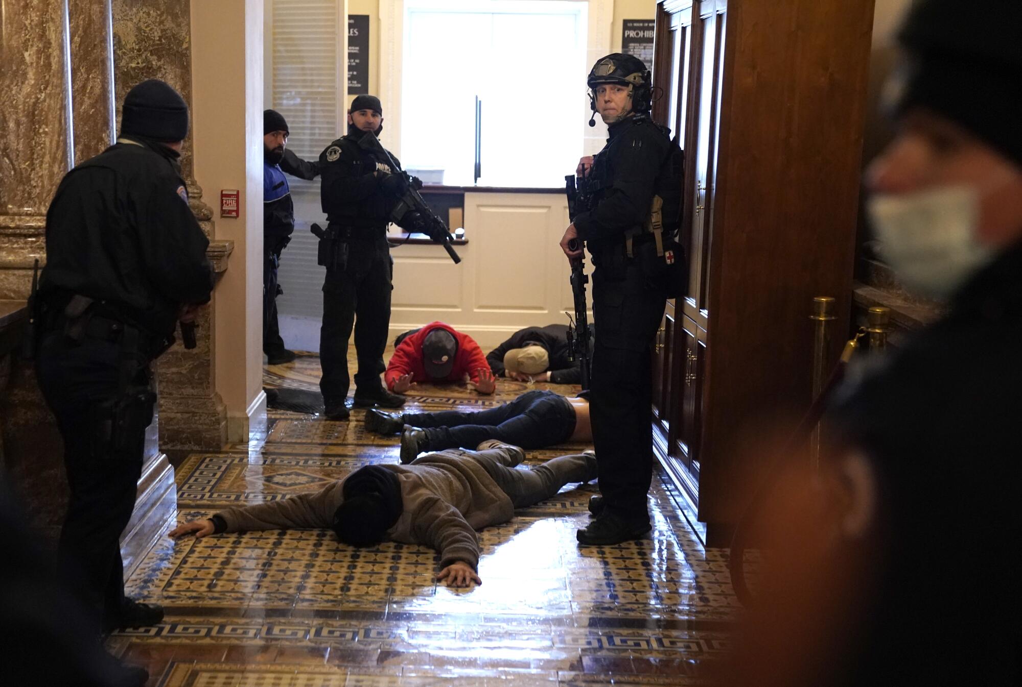 Police hold guns on several people lying face down on the floor in a Capitol hallway.