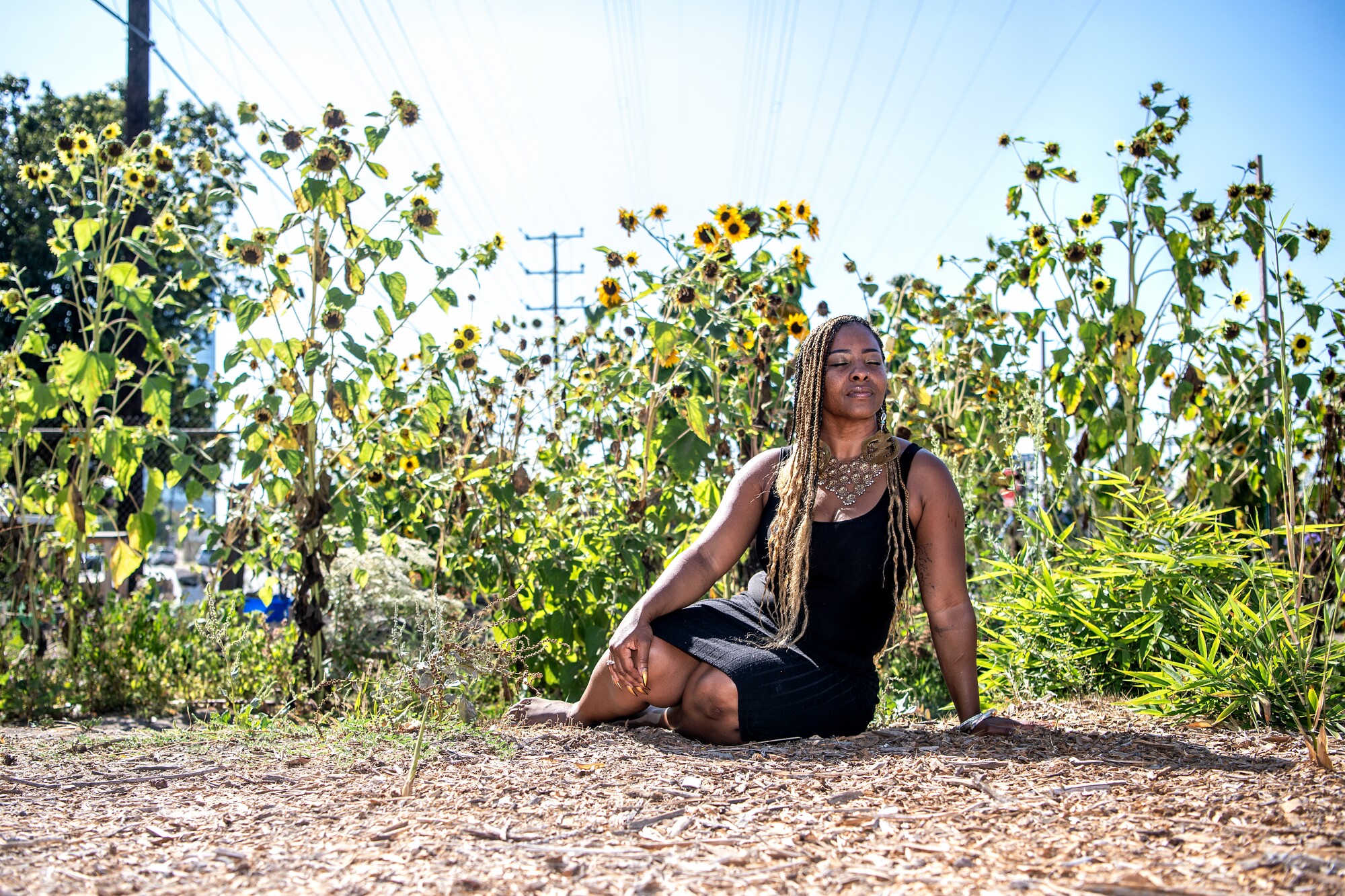 Genea Richardson sits on the ground in a garden, surrounded by sunflowers.