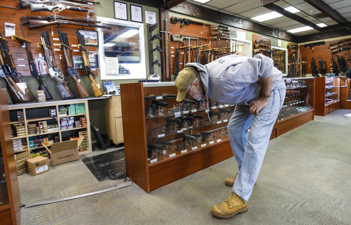 A man bends over in a gun store to look at merchandise in a cabinet.