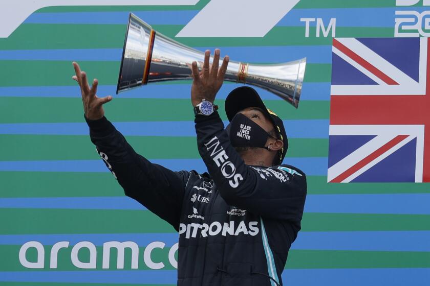 Mercedes driver Lewis Hamilton of Britain throws the trophy in the air at the podium as he celebrates after winning the Eifel Formula One Grand Prix at the Nuerburgring racetrack in Nuerburg, Germany, Sunday, Oct. 11, 2020. Hamilton with this win equals 91 wins in F1 races as F1 legend Michael Schumacher. Red Bull driver Max Verstappen of the Netherlands finished second and Renault driver Daniel Ricciardo of Australia finished third. (Ronald Wittek, Pool via AP)