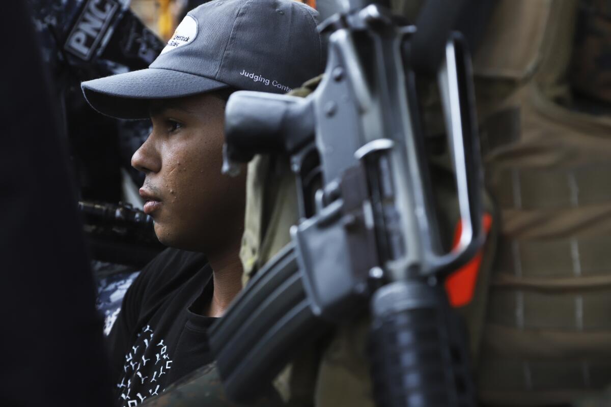 Armed police surround a young man in a baseball hat.