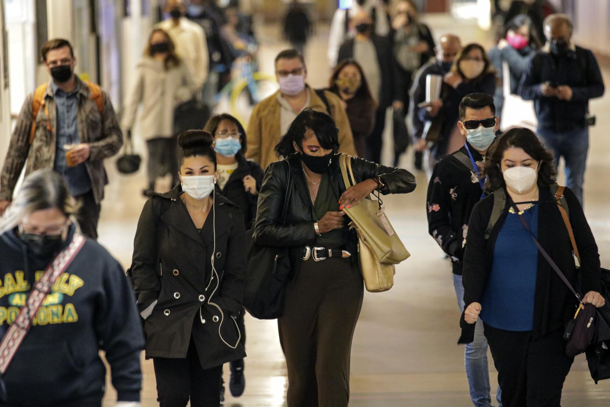 People wearing masks walk through a subway station