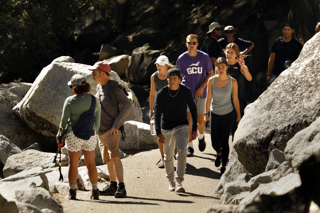 About 10 hikers walk on a trail between boulders and rocks