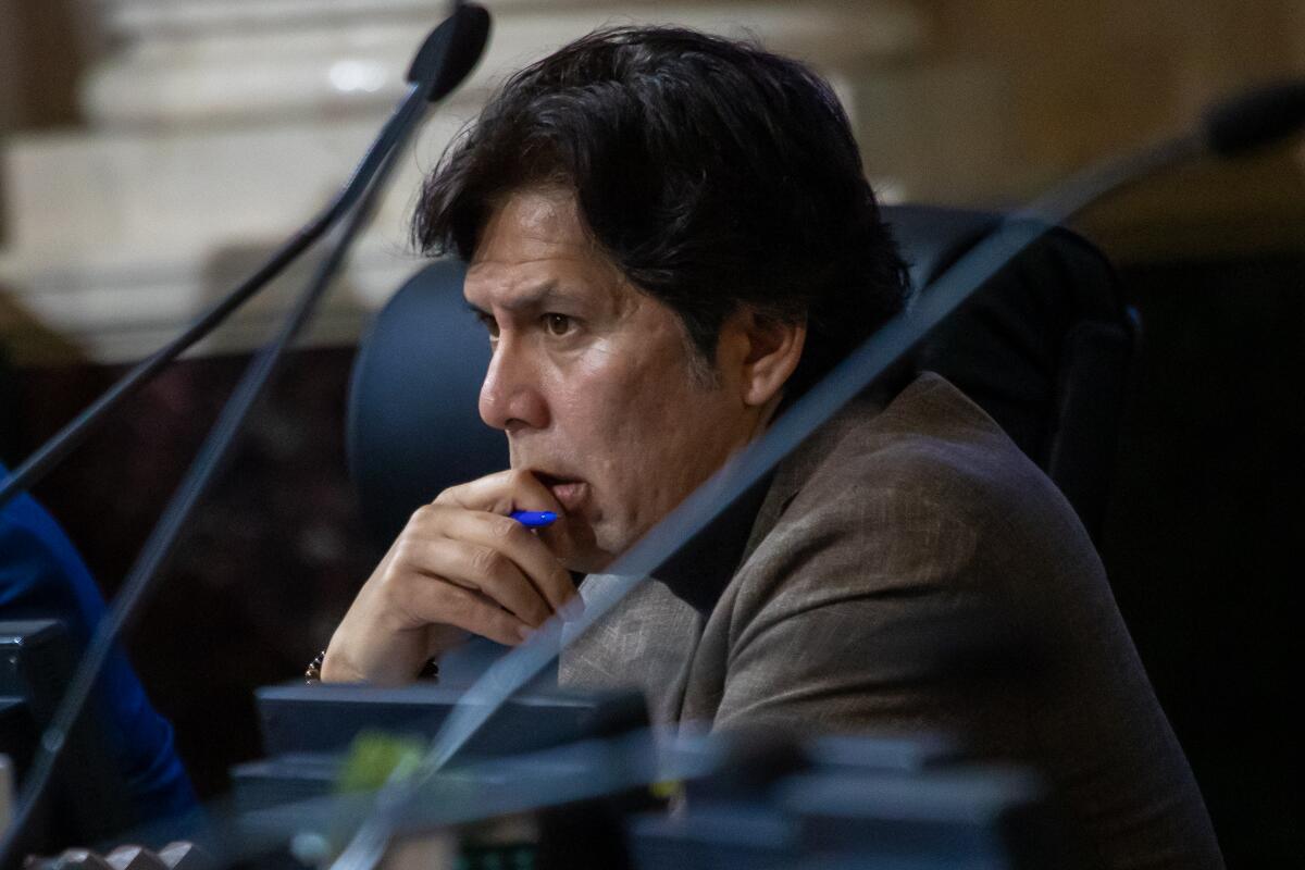 Councilmember Kevin de León seen in profile, leaning his chin against his right hand, which is holding a blue pen.