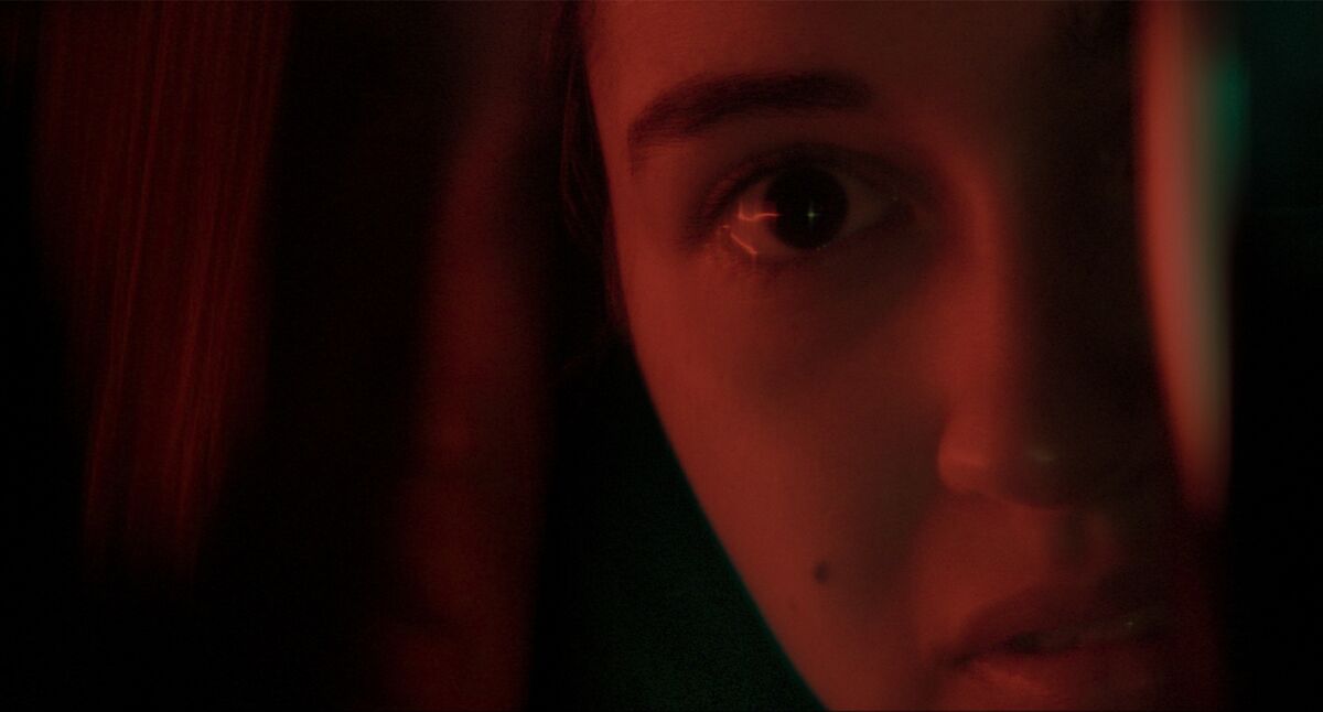 A close up of the face of a girl bathed in dark red light.