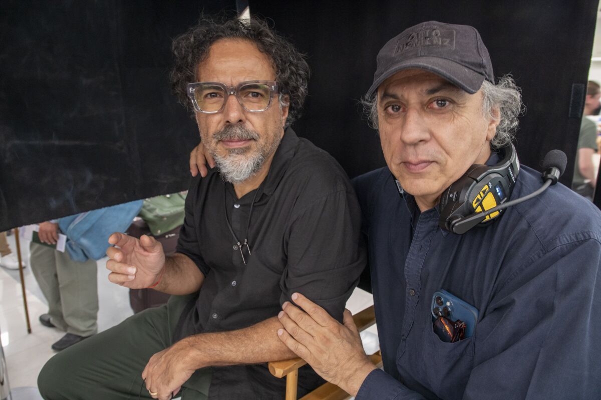 Two men in director's chairs pose for a portrait on a movie set.
