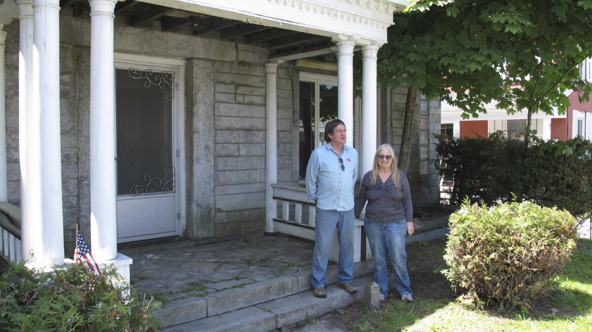 Brian and Joan Dumoulin pose on both sides of a marker showing the U.S.-Canadian border in the front yard of their home on June 8 in Derby, Vt. She is in Canada, and he is in the United States.