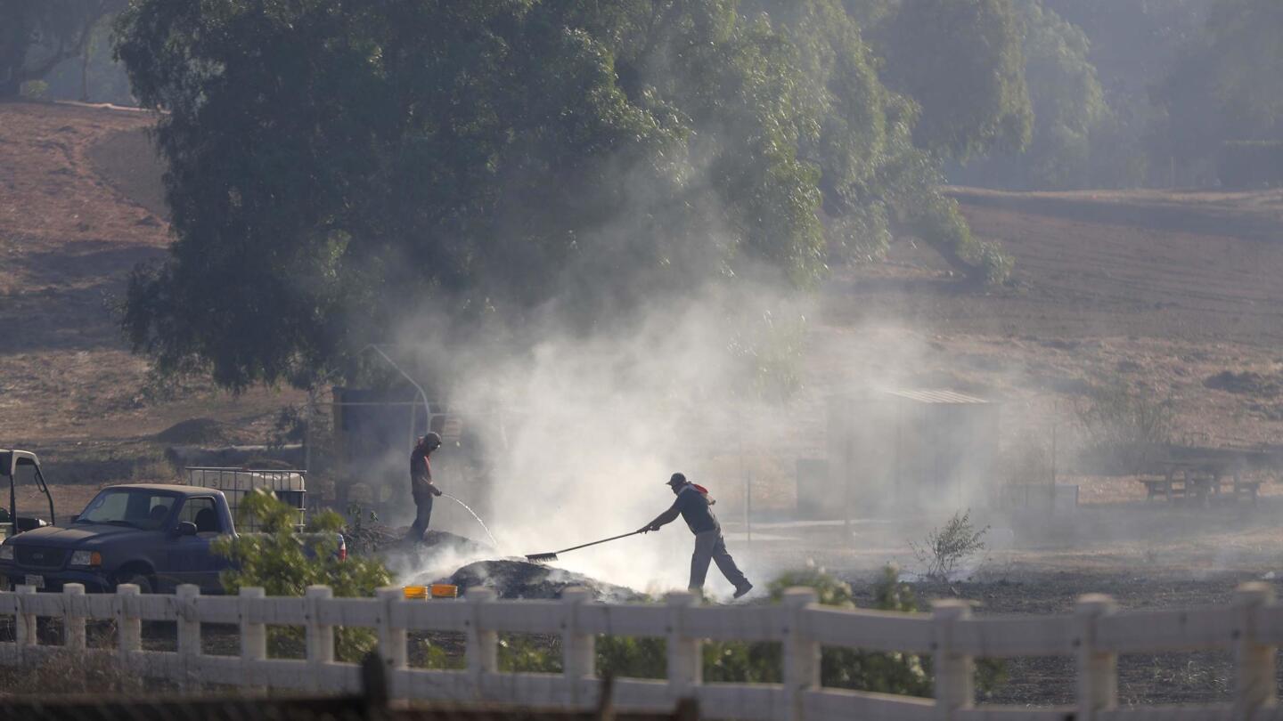 Workers work to put out a smoldering fire along West Lilac Road.