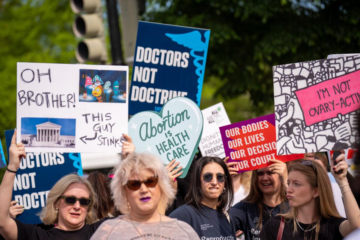 People hold signs reading "Doctors not doctrine" and "Abortion is healthcare."
