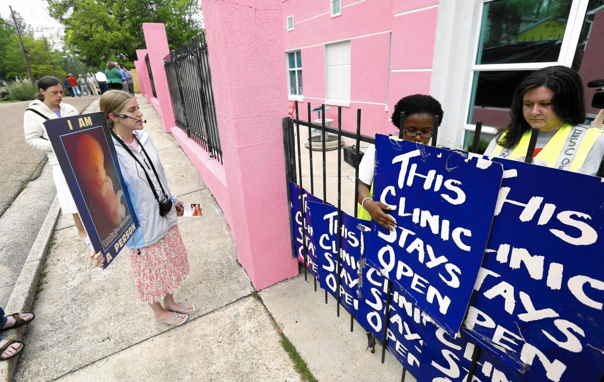 Abortion opponents demonstrate outside a clinic in Jackson, Miss., in 2013, while clinic employees secure signs to the front gate to help hide patients from protesters' view.