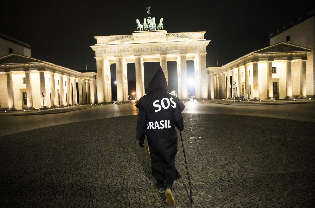 Brazilian activist and artist Rafael Puetter, dressed as the grim reaper, walks in front of the Brandenburg Gate in a one-man protest through Berlin, Germany, early Wednesday, April 7, 2021. The multimedia artist starts his performance at the Brazilian embassy in Berlin at midnight every night to protest against Brazil's COVID-19 policies. Rafael Puetter walks to the Brandenburg Gate and then to the nearby German parliament building, in front of which he counts out a sunflower seed to represent each of the lives that were lost over the past 24 hours in Brazil because of the coronavirus pandemic. (AP Photo/Markus Schreiber)