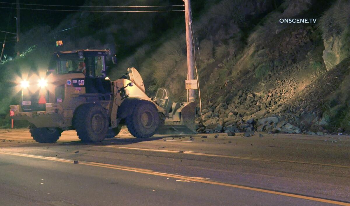 A front loader clears rocks from a road at night.