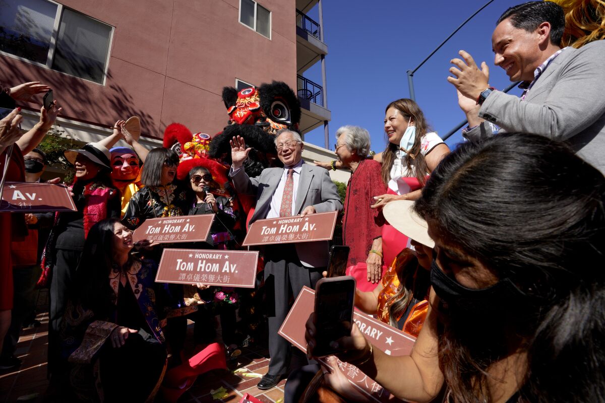 Tom Hom holds his honorary street sign and waves while surrounded by friends and family.