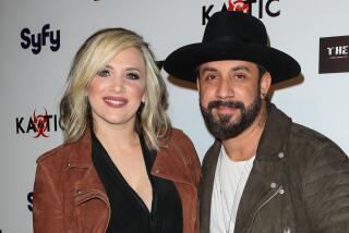 AJ McLean, in a brown jacket and black wide brim hat, poses with Rochelle McLean, in a light-brown jacket, black shirt